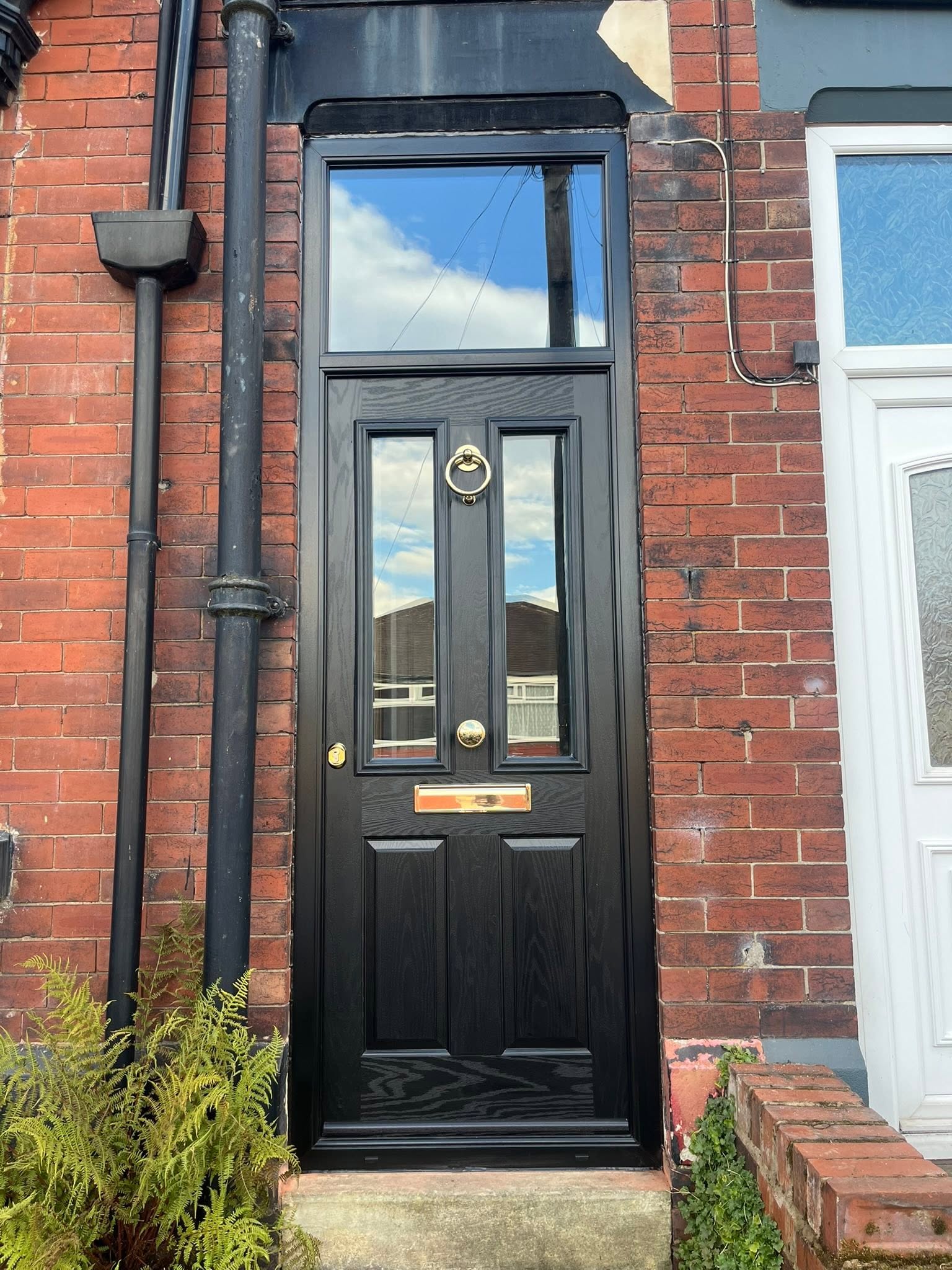 Black composite front door with brass furniture on a red brick terrace
